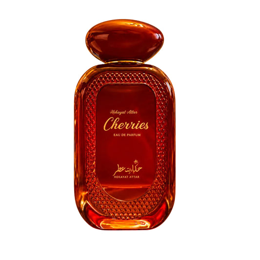 A bottle of hekayat attar Cherries Eau de Parfum in a textured amber-red glass bottle with a matching cap, shown next to travel atomizer spray vials on a white background.